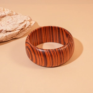 Close-up of wide wooden bangle with natural dark grain textures against stone decor
