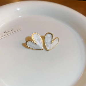 Macro view of gold heart stud earrings with pearlescent white inlay on white ceramic
