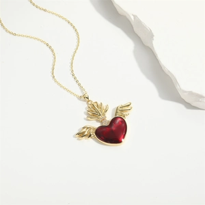 Macro detail of winged heart pendant with red enamel inlay and gold chain necklace
