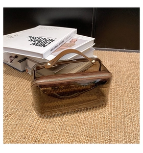 Detail der transparenten braunen PVC-Kosmetiktasche mit Ledergriff auf Webmatte
