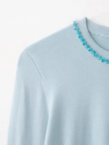Close-up of light blue knit sweater featuring floral rhinestone neck embellishment
