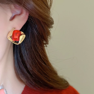 Detail of a vintage-style earring with red square gemstone in twisted gold metal frame