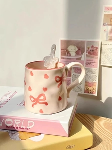 Detail of beige ceramic mug with pink bow heart pattern and star-shaped spoon