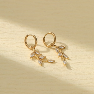 Golden titanium steel leaf earrings with clear zircon crystals on a textured background