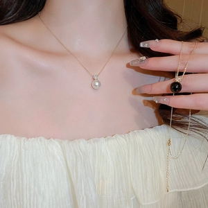 Close-up of minimalist gold chain necklace with round pearl and sparkling zircon pendant