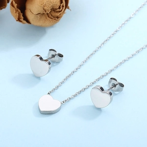 Flat lay of heart-shaped necklace and stud earring set on light blue background
