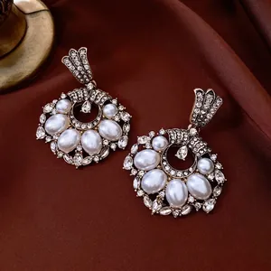 Vintage gold drop earrings with pearls and rhinestones on dark red silk background
