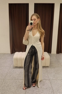 Close-up of cream knit long vest with deep V-neck and high side slits on casual outfit