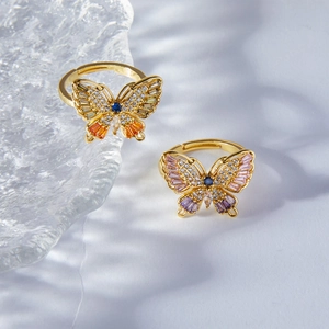 Elegant gold butterfly rings with colorful gemstones on a textured glass surface