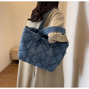 Sac cabas matelassé en jean bleu porté par un mannequin dans un décor épuré