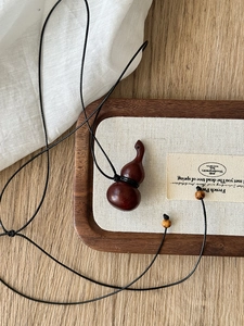 Macro view of wooden gourd pendant with wooden beads and black woven cord on wood tray