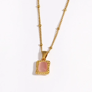 Detailopname van een gouden ketting met een roze stenen hanger en gehamerd metalen frame