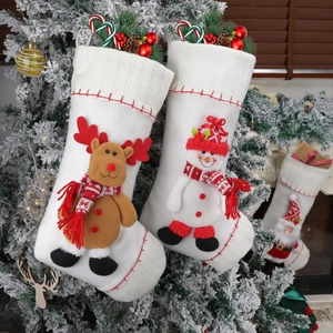 White knitted Christmas stockings with 3D reindeer and snowman hanging on a snowy tree