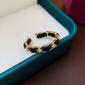 Dettaglio macro di un anello aperto placcato oro con pelle intrecciata nera e zirconi brillanti
