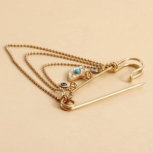 Detail of gold safety pin brooch with layered chains and blue crystal evil eye charms