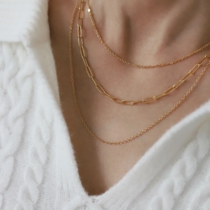 Detailed view of triple-layered gold necklaces paired with a white knit sweater