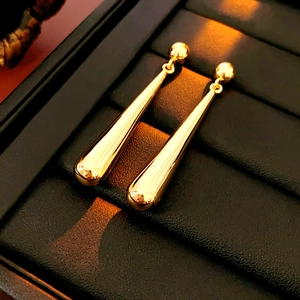 Macro shot of long gold teardrop earrings displayed on black leather texture