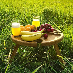 Portable wooden round picnic table with wine glass holder on sunny outdoor lawn