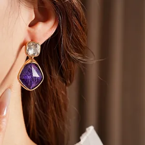 Vintage brushed gold drop earrings with purple faceted stones worn by a model