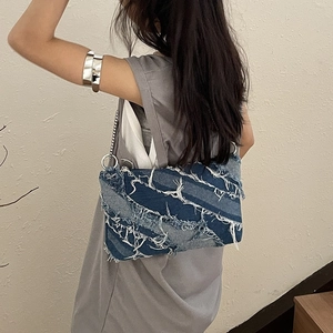 Washed denim crossbody bag with fringe details and silver chain strap shown on model