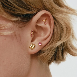 Minimalist gold hoop earrings set with pink zircon stones worn on female ear model