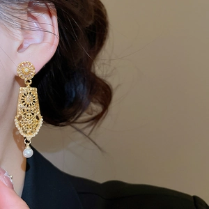 Close-up of vintage hollow geometric earrings with gold finish and white pearl drop detail