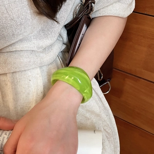 Close-up of a wide green acrylic cuff bracelet with marble texture worn by a model