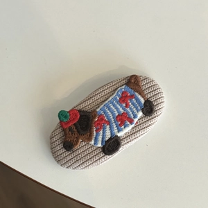 Detail of a handmade knitted dachshund hair clip with striped sweater and red bow