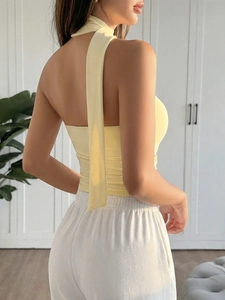 Detail showing the side-back view of a yellow halter neck backless top on a model