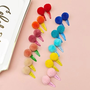 Close-up of 20 colorful plush ball drop hair clips arranged on a soft pink surface
