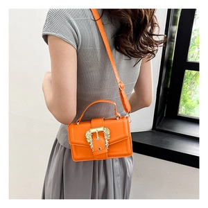 Orange crossbody bag with ornate gold baroque buckle shown on model for scale