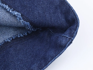Macro shot of dark blue twill denim fabric detailing the frayed edge and raw hem texture