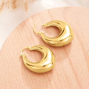 Close-up of chunky gold teardrop hoop earrings on a light wood tray with dried plants