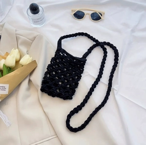 Detail view of a black woven mini crossbody bag styled with trendy fashion accessories