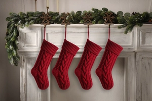 Detailed view of four red cable knit Christmas stockings hanging on a festive white fireplace