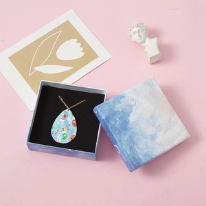 Detail of drop-shaped gold necklace with Christmas sock motif in marble gift box