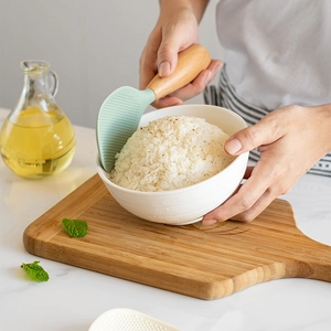 Standing silicone rice paddle with mint green head and wood handle in a bowl of white rice