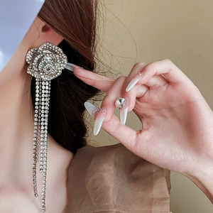 Détail de boucles d'oreilles fleur argentée avec strass et pompon portées par un modèle