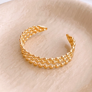 Detail view of gold three-layer beaded open cuff bracelet resting in a ceramic bowl