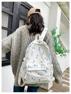 Detail of white canvas backpack with blue tulip pattern worn by a model on the back