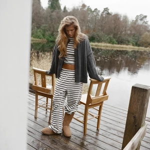 Detail of striped lounge set and grey knit cardigan worn with boots on a lakeside dock