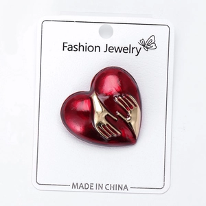 Close-up of a red enamel heart brooch with gold hugging hands on white card