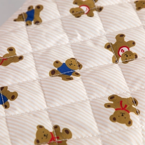 Detailed macro view of quilted cream fabric featuring cute hand-drawn cartoon bear patterns