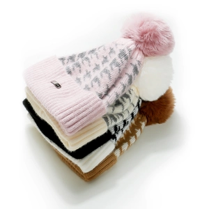 Dettaglio di berretti invernali in maglia leopardata con pompon in pelliccia e logo in metallo