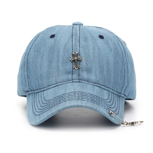 Blue denim baseball cap with metal cross emblem and safety pin pendant on brim