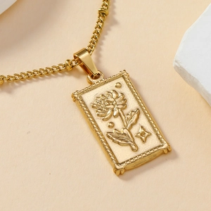 Collana con ciondolo quadrato dorato, motivo floreale e stelle su sfondo beige neutro
