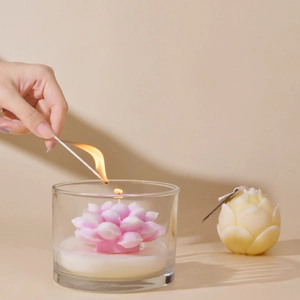 Candela a loto rosa in vetro e candela a bocciolo giallo con mano che accende un fiammifero