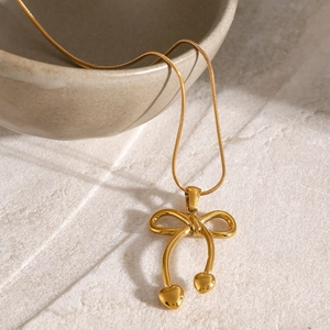 Detailed shot of a gold bow and heart pendant necklace on a modern ceramic bowl