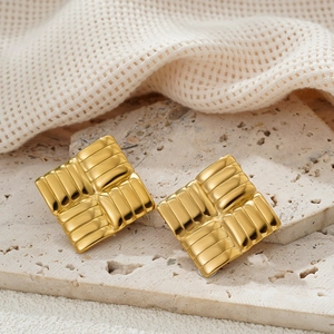 Close-up of golden square earrings with woven texture on a natural stone surface