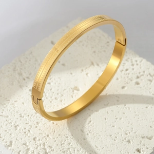 Armreif aus Titanstahl in Gold mit geometrischer Gravur auf weißem Steinuntergrund
